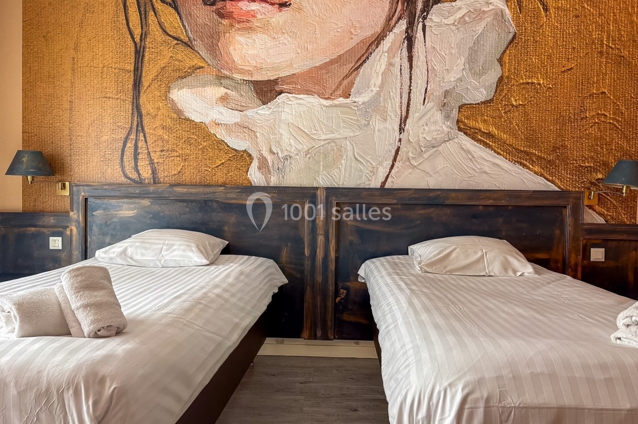 Deux lits simples avec draps blancs, appuyés contre un mur décoré d'une peinture murale artistique.