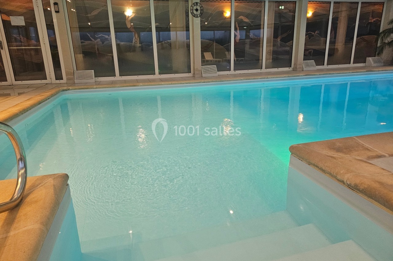 Piscine intérieure éclairée avec des marches en pierre, entourée de baies vitrées donnant sur un espace extérieur.