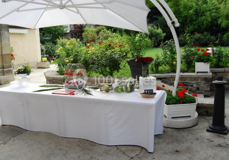 Table dressée sous un parasol blanc dans un jardin fleuri, avec des décorations et des éléments de buffet.