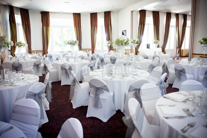 Salle de réception élégante avec tables rondes dressées, nappes blanches et chaises décorées de nœuds gris.