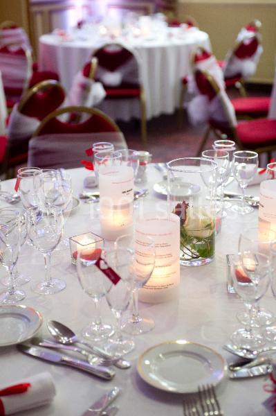 Table élégamment dressée avec nappes blanches, verres, couverts, bougies et décorations florales dans une salle de réception.