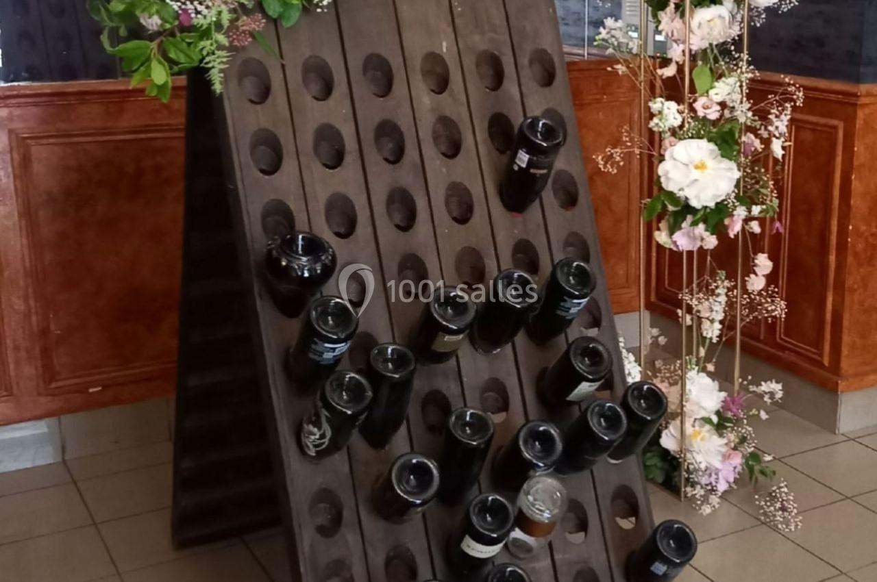 Support en bois incliné avec des bouteilles en verre insérées, entouré de décorations florales.