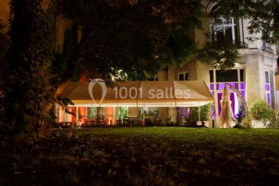 Salle vide avec moquette, tables hautes noires et une longue table blanche près des fenêtres avec rideaux.