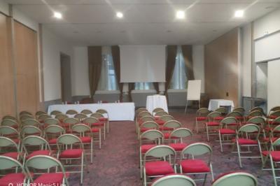 Salle vide avec moquette, tables hautes noires et une longue table blanche près des fenêtres avec rideaux.