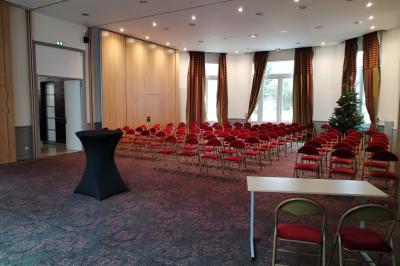 Salle vide avec moquette, tables hautes noires et une longue table blanche près des fenêtres avec rideaux.