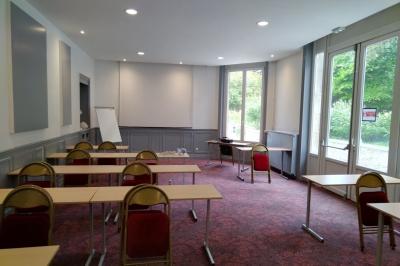 Salle vide avec moquette, tables hautes noires et une longue table blanche près des fenêtres avec rideaux.