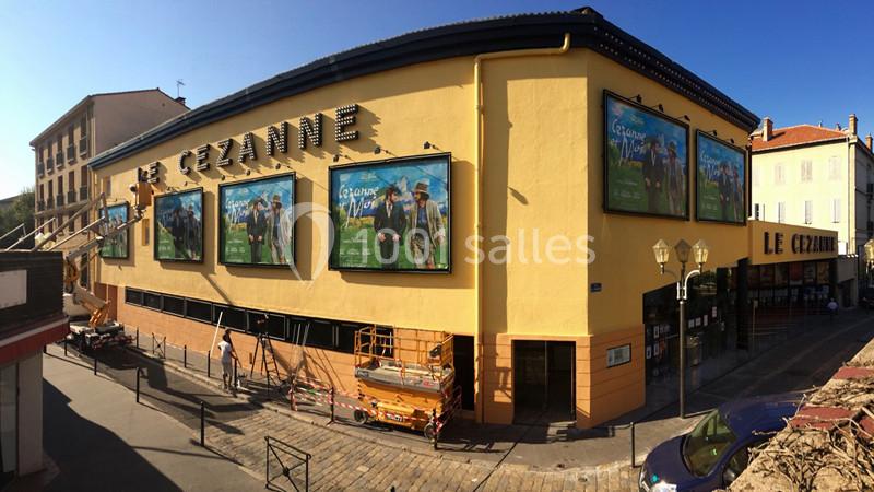 Façade d'un cinéma jaune avec plusieurs affiches de films, situé dans une rue ensoleillée.