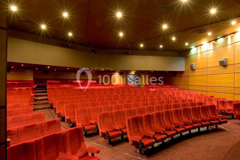 Salle de cinéma vide avec rangées de sièges rouges, murs en bois clair et éclairage au plafond.