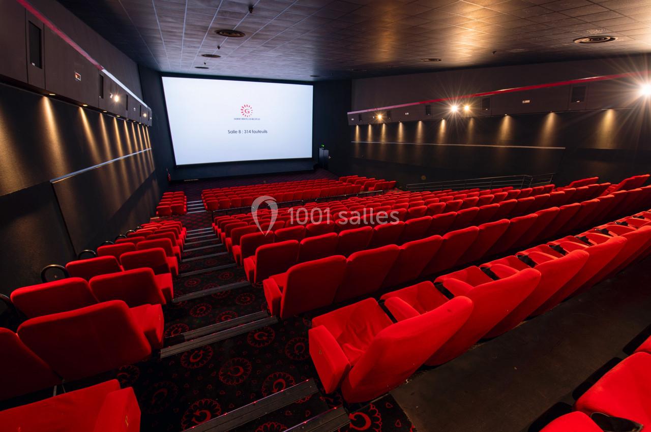 Salle de cinéma vide avec des rangées de fauteuils rouges et un grand écran blanc au fond.