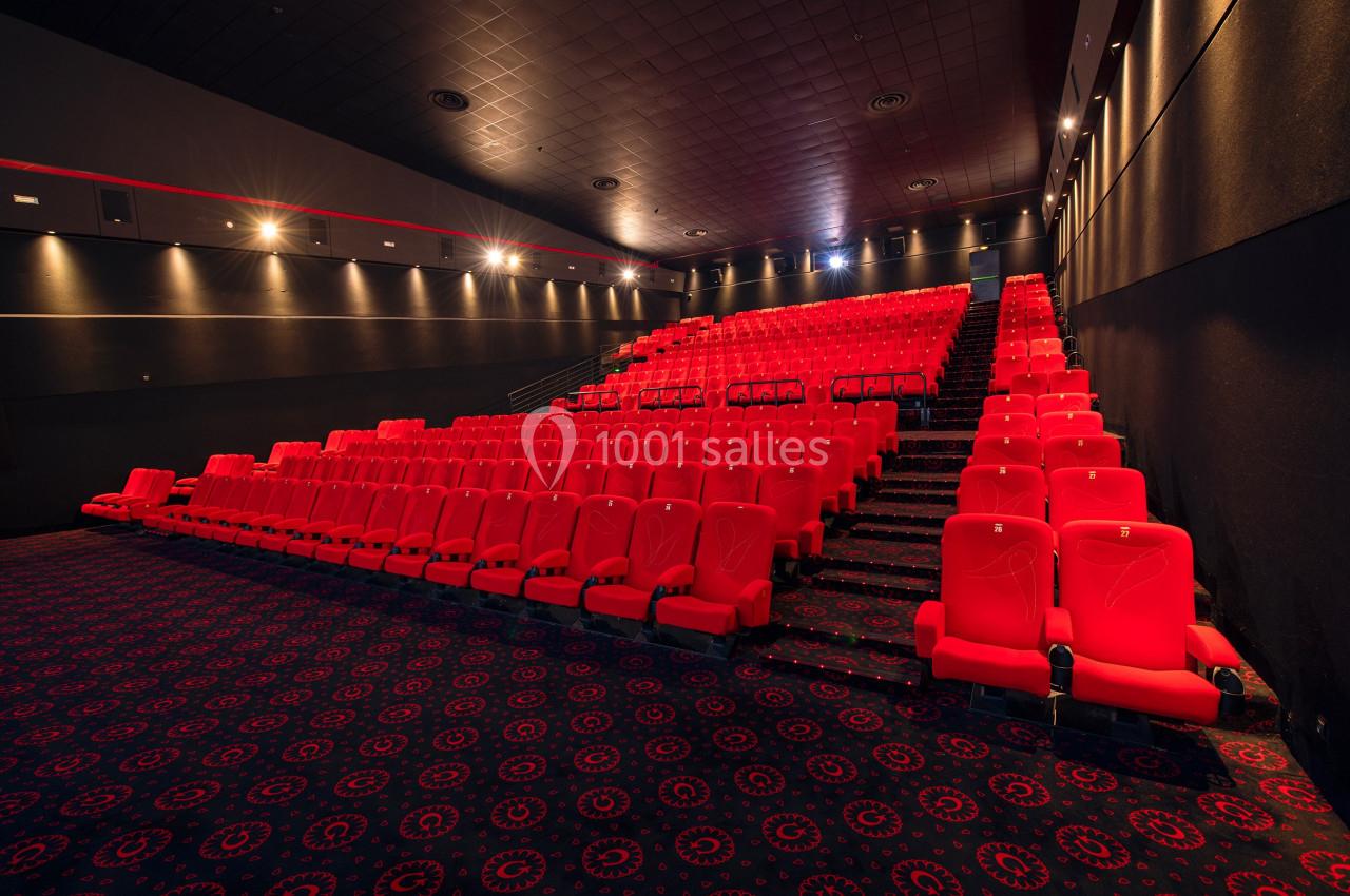 Salle de cinéma vide avec des rangées de sièges rouges et un sol recouvert de moquette à motifs.