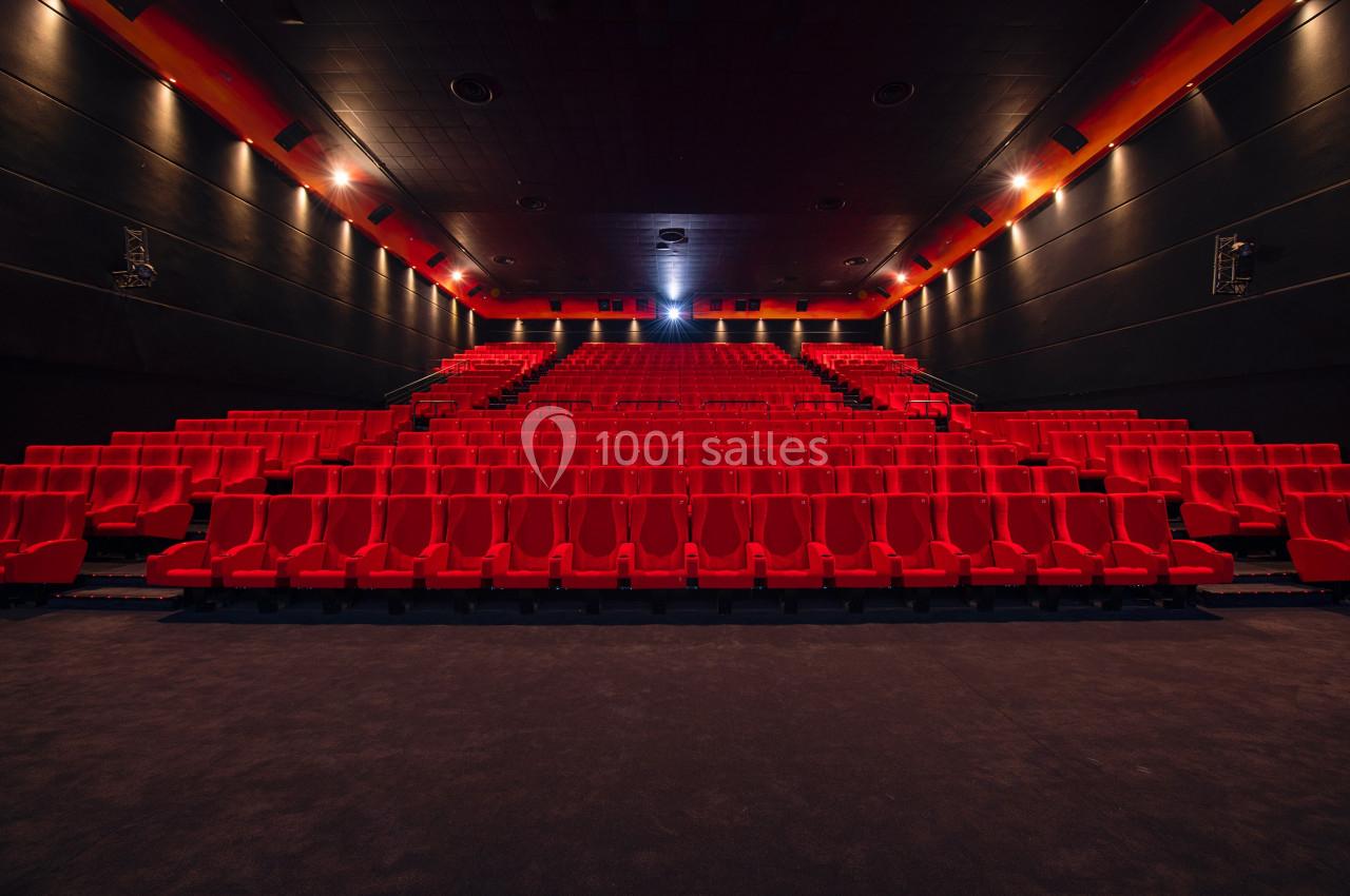 Salle de cinéma vide avec des rangées de sièges rouges et un écran éteint au fond.