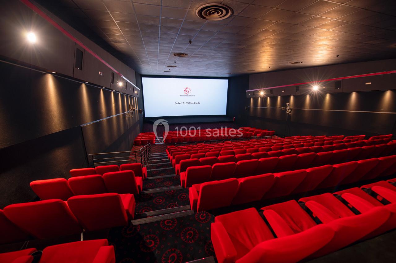 Salle de cinéma vide avec rangées de sièges rouges et écran blanc allumé dans un espace sombre.