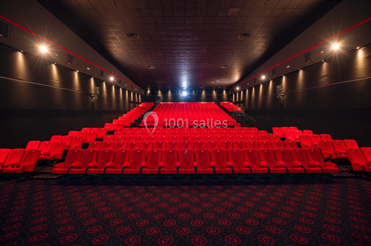 Salle de cinéma vide avec rangées de sièges rouges, éclairage tamisé et écran en arrière-plan.