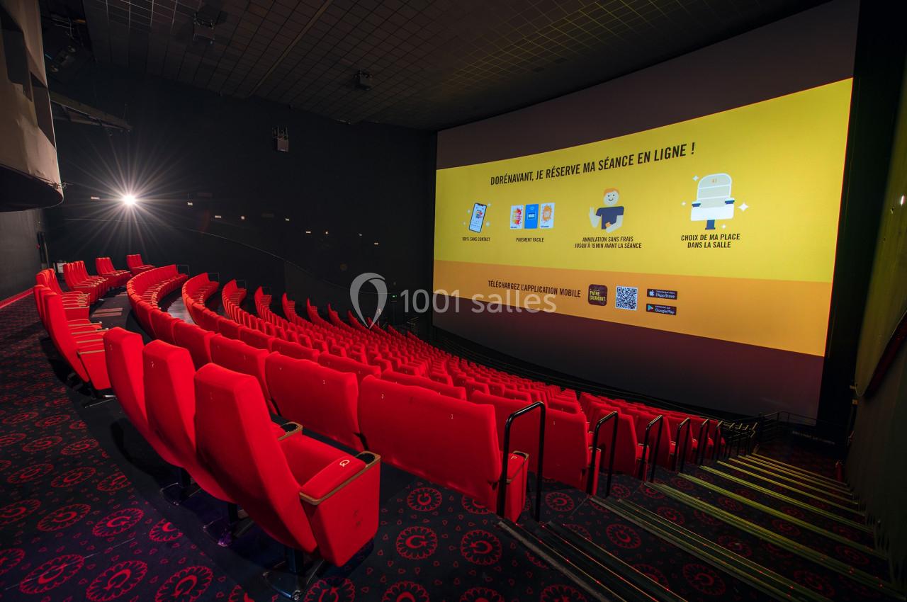 Salle de cinéma vide avec des sièges rouges alignés et un écran affichant des instructions pour réserver en ligne.