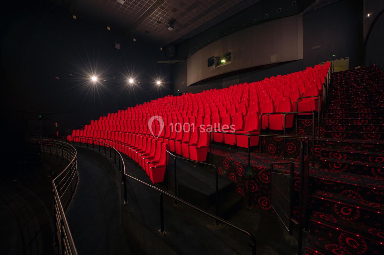 Salle de cinéma vide avec des rangées de sièges rouges et un éclairage tamisé.