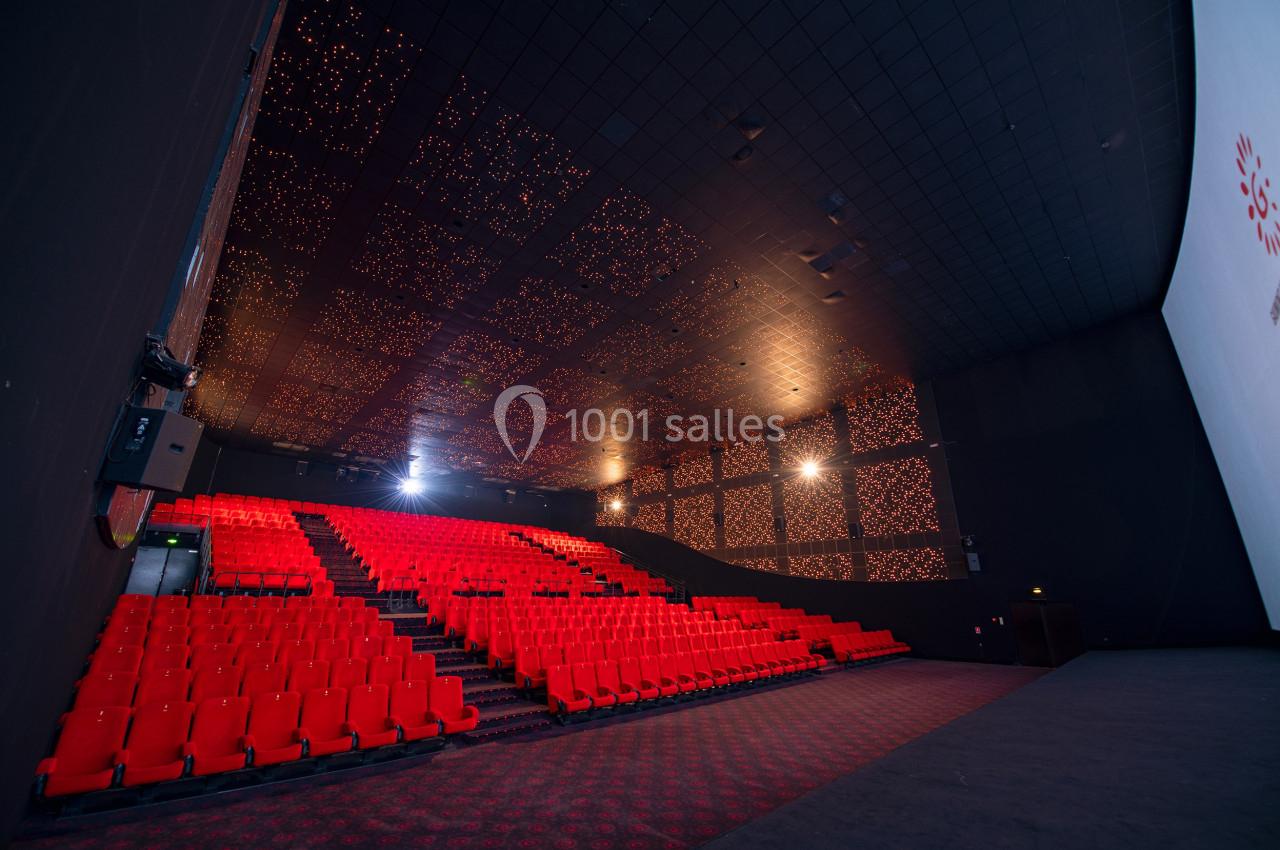 Salle de cinéma vide avec sièges rouges, écran blanc et plafond décoré de lumières.