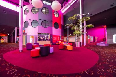 Vue extérieure d'un complexe IMAX moderne avec une esplanade dégagée et un ciel partiellement nuageux.