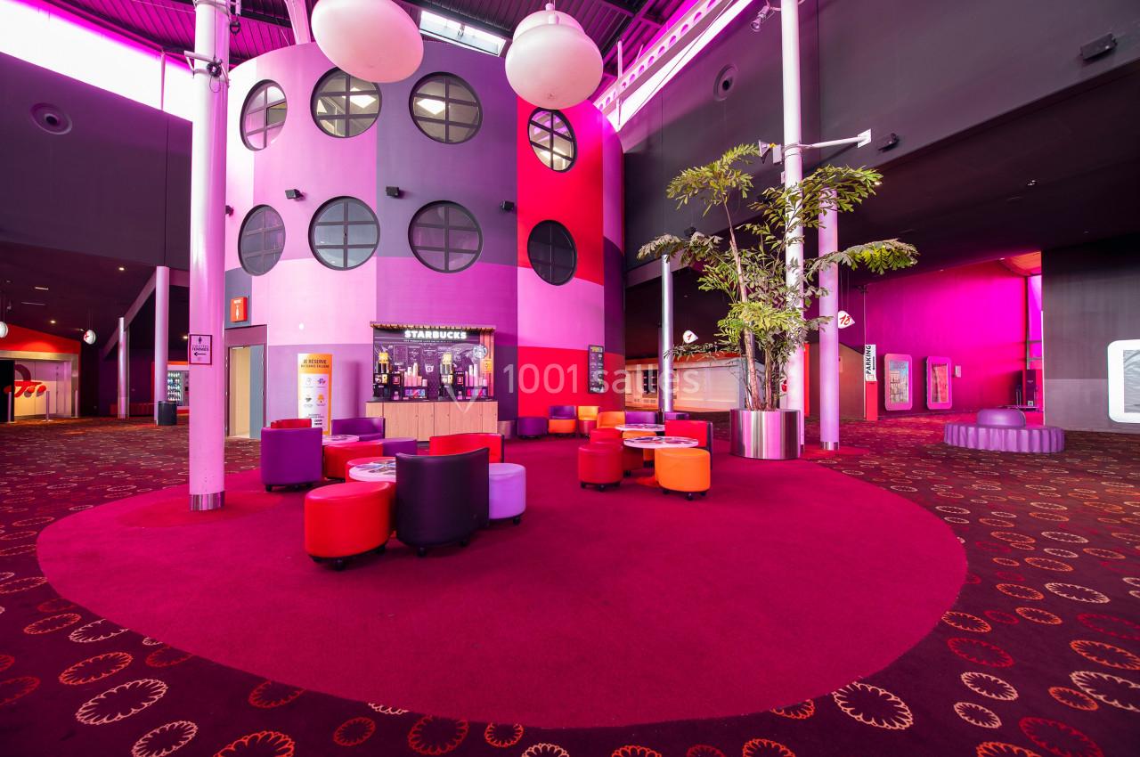 Espace intérieur coloré avec fauteuils rouges et violets, sol moquetté et décorations lumineuses modernes.