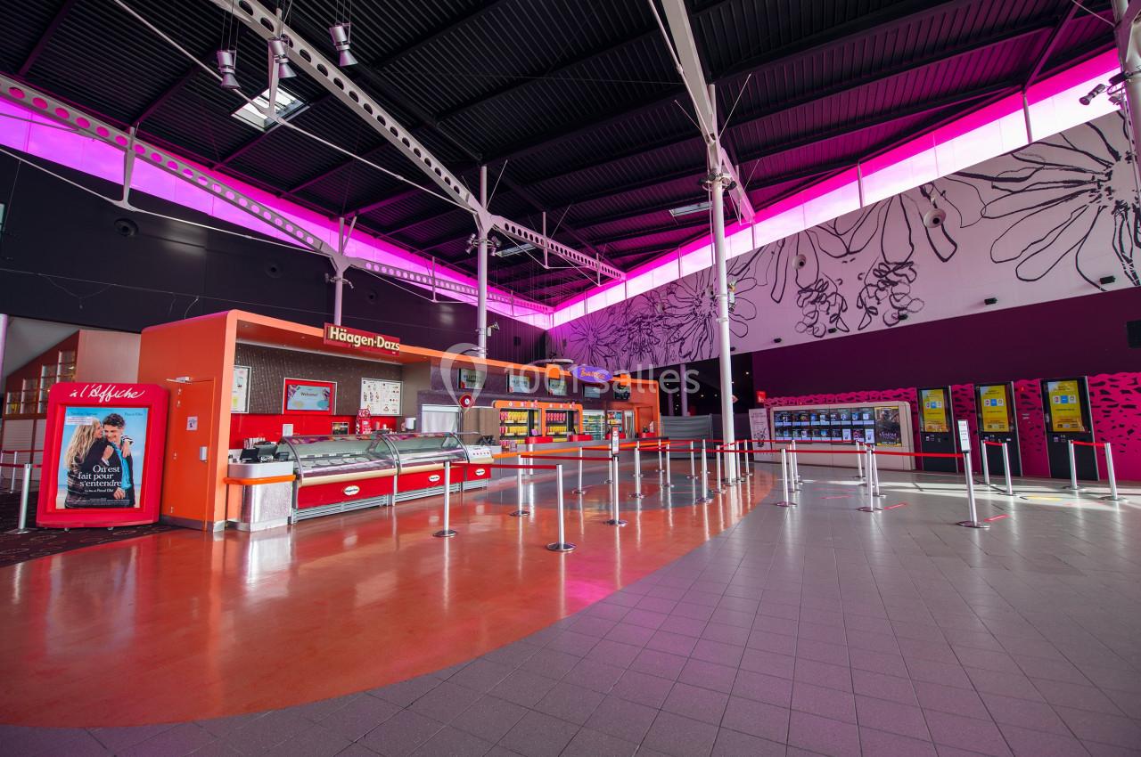 Comptoir de glaces et snacks dans un espace lumineux avec décorations murales et éclairage rose au plafond.