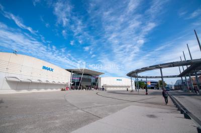 Vue extérieure d'un complexe IMAX moderne avec une esplanade dégagée et un ciel partiellement nuageux.