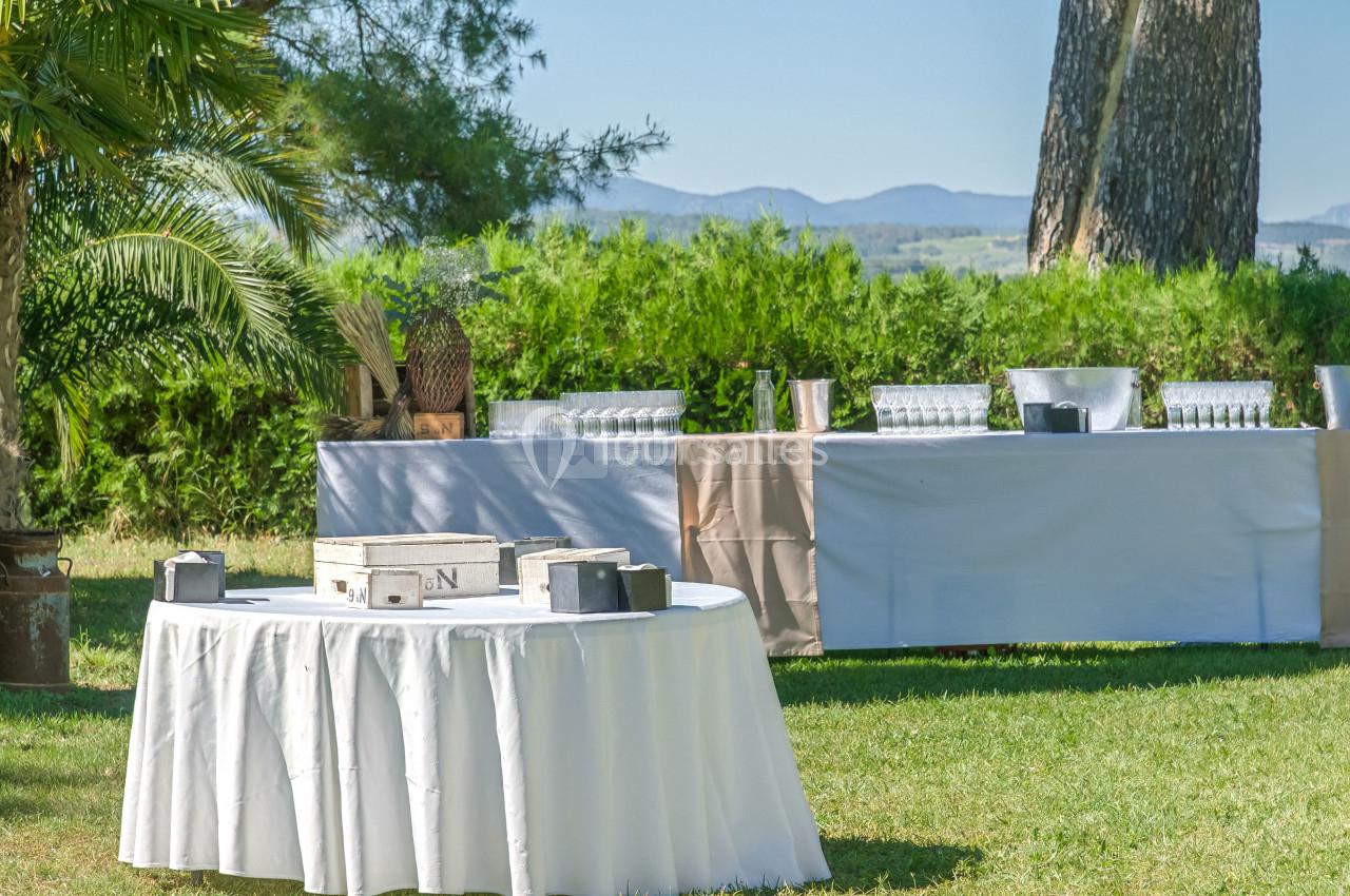 Tables dressées en extérieur avec nappes blanches, verres et décorations, entourées de verdure et d'arbres.