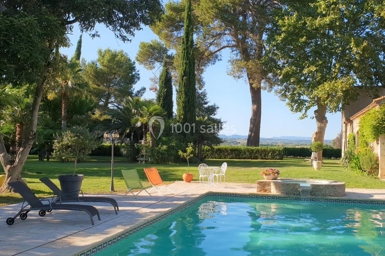 Jardin arboré avec piscine, transats et mobilier de jardin, entouré de verdure sous un ciel dégagé.