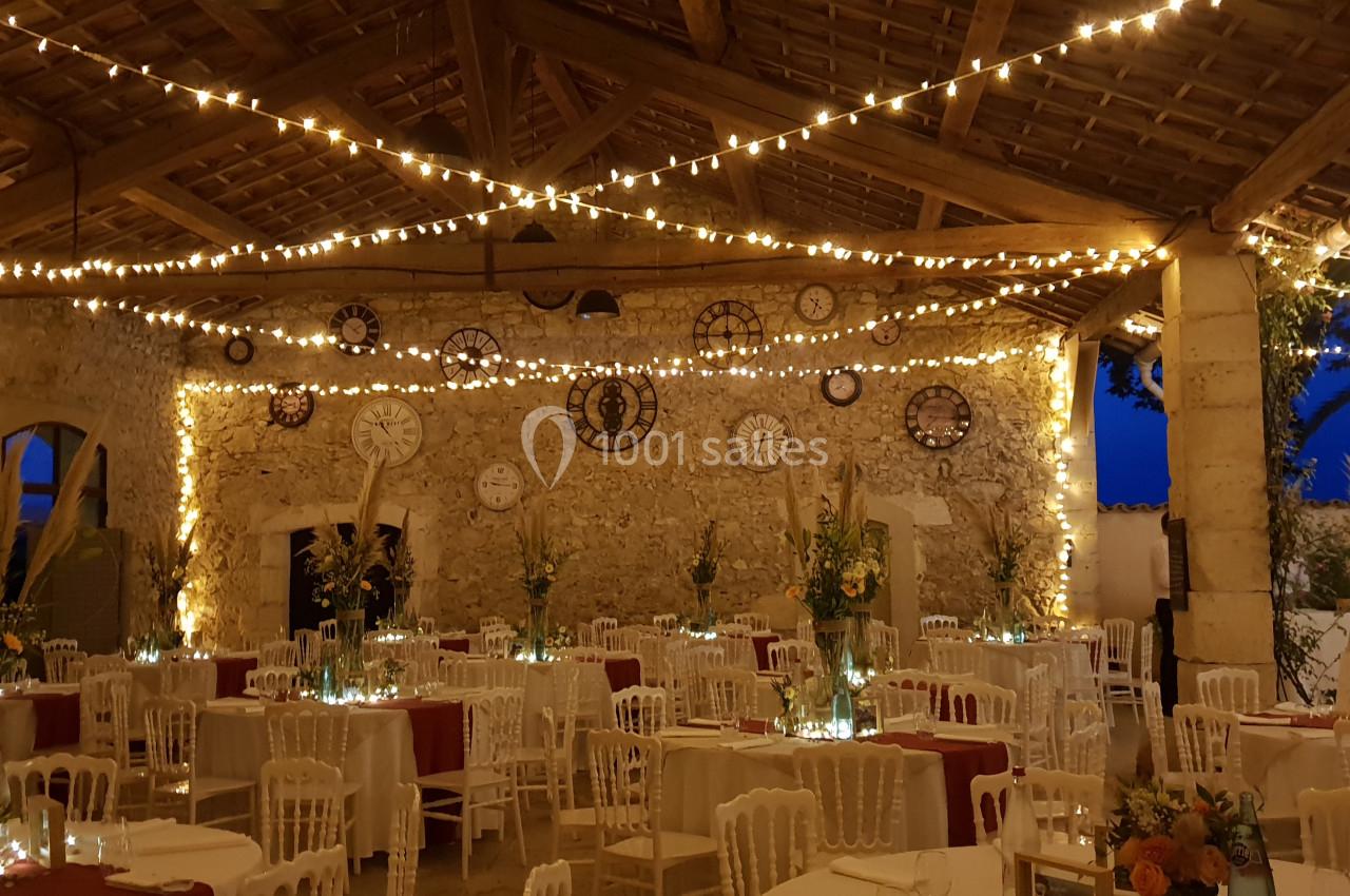 Salle en pierre décorée de guirlandes lumineuses, tables dressées avec nappes rouges et arrangements floraux.