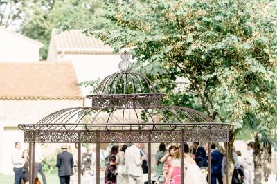 Structure en fer forgé dans un jardin, avec des invités rassemblés en arrière-plan près d'un arbre.
