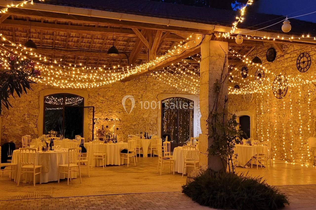 Salle de réception en soirée avec tables dressées et guirlandes lumineuses décorant murs et plafond.
