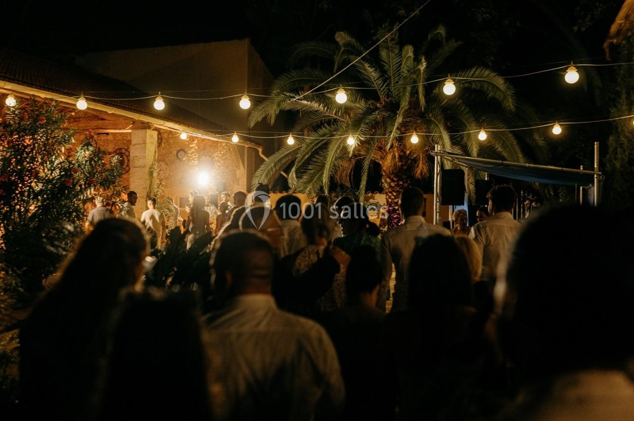 Groupe de personnes rassemblées en soirée sous des guirlandes lumineuses, près de palmiers et d'un bâtiment éclairé.