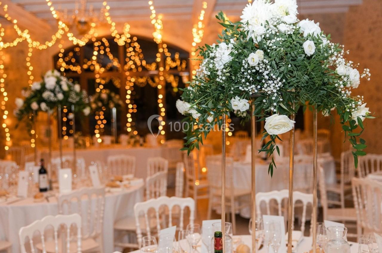 Salle de réception décorée avec des guirlandes lumineuses, des tables dressées et des centres de table fleuris.