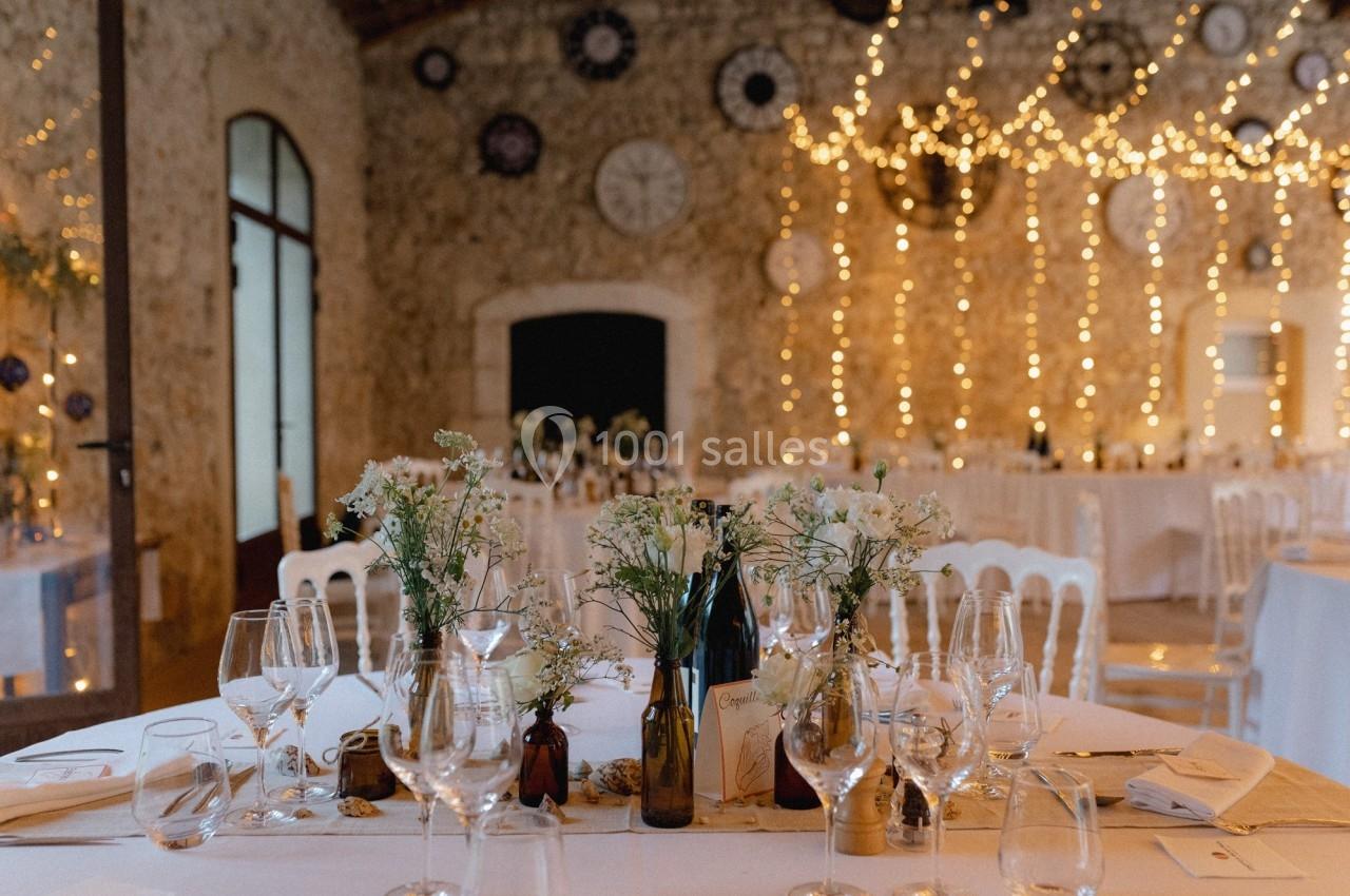 Salle de réception décorée avec des guirlandes lumineuses, des tables dressées et des fleurs en centre de table.