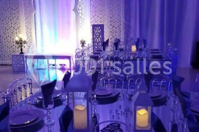 Table garnie de pâtisseries et de desserts variés, éclairée par une lumière rose et violette dans un décor festif.