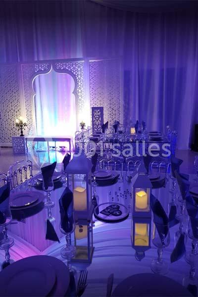 Salle de réception décorée avec des lanternes, des tables dressées et un éclairage violet créant une ambiance élégante.