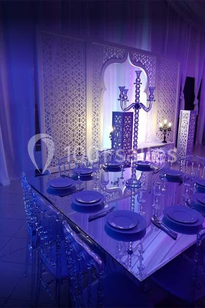Table élégante dressée avec vaisselle blanche et chaises transparentes, décorée d'un chandelier, dans une ambiance lumineuse…