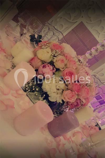 Bouquet de fleurs roses et blanches entouré de bougies pastel sur une table décorée pour un événement.