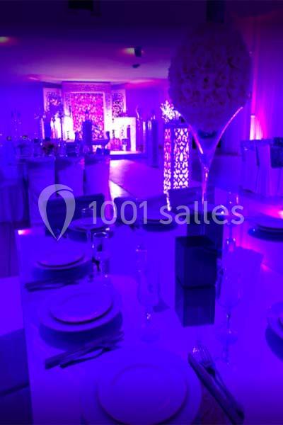 Salle de réception décorée avec des tables dressées et un éclairage violet tamisé.