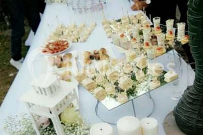 Table garnie de pâtisseries et de desserts variés, éclairée par une lumière rose et violette dans un décor festif.