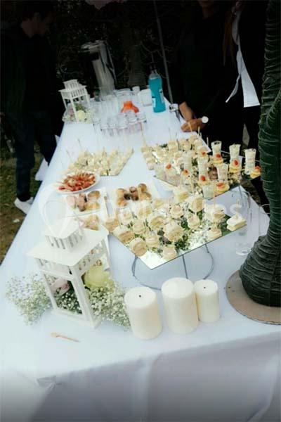 Table dressée avec des amuse-bouches variés, bougies blanches et décorations florales, en extérieur.