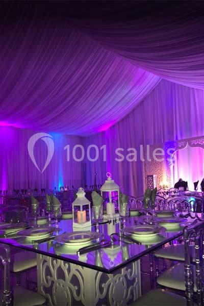 Salle de réception décorée avec des tables élégantes, des lanternes blanches et un éclairage violet tamisé.