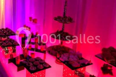 Table garnie de pâtisseries et de desserts variés, éclairée par une lumière rose et violette dans un décor festif.