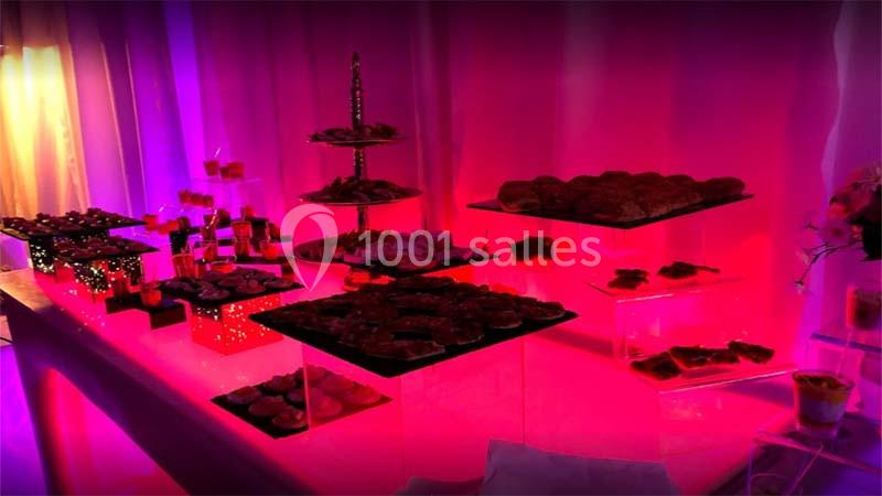 Table de buffet éclairée par des lumières roses et violettes, présentant divers plats et desserts sur des présentoirs.