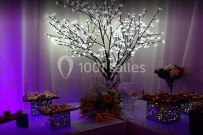 Table garnie de pâtisseries et de desserts variés, éclairée par une lumière rose et violette dans un décor festif.