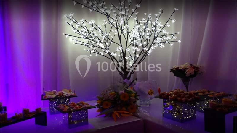 Table décorée avec un arbre lumineux, des fleurs et des plateaux de petits fours dans une ambiance éclairée en violet.