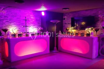 Table garnie de pâtisseries et de desserts variés, éclairée par une lumière rose et violette dans un décor festif.