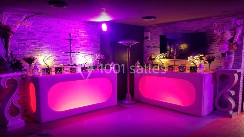 Salle décorée avec des lumières roses, deux comptoirs lumineux, des fleurs et des éléments décoratifs modernes.