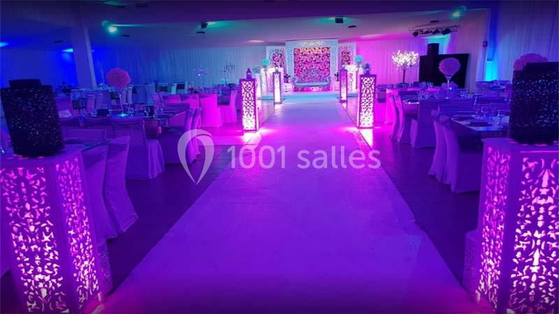 Salle de réception décorée avec des tables dressées, un éclairage violet et une allée centrale illuminée.