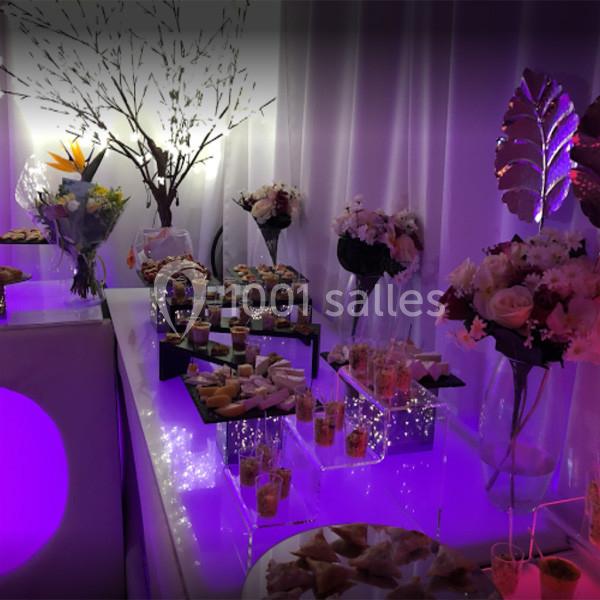 Buffet décoré avec des fleurs, des lumières violettes et des amuse-bouches disposés sur des présentoirs élégants.