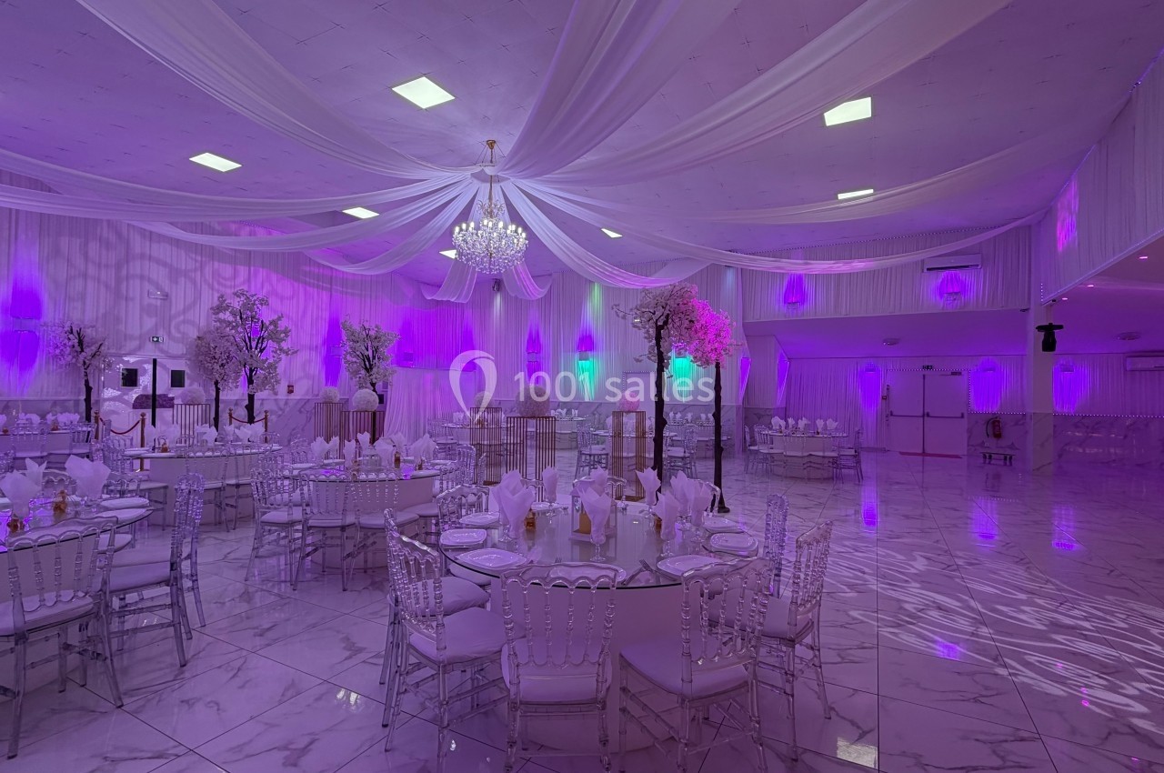 Salle de réception élégamment décorée avec des tables dressées, éclairage violet et plafond drapé.