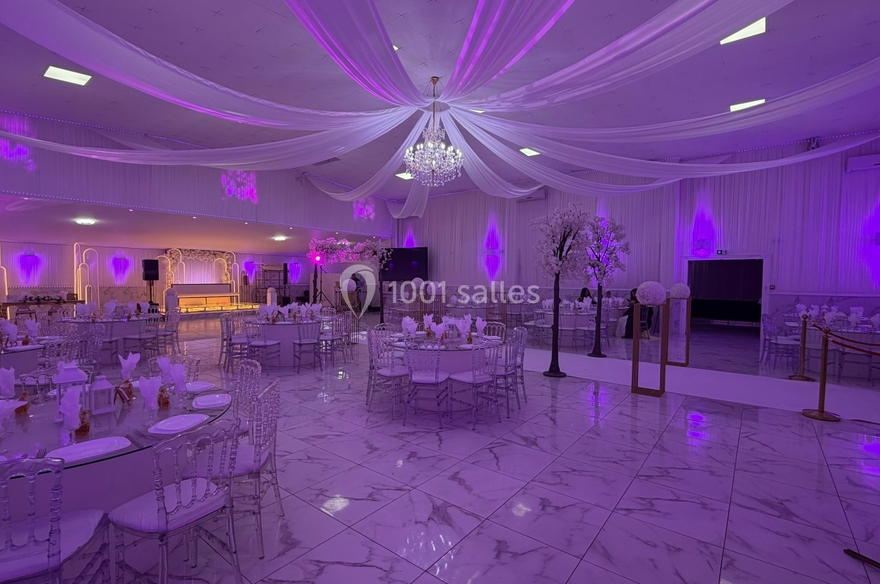 Salle de réception élégante avec tables dressées, éclairage violet, plafond drapé et lustre central.